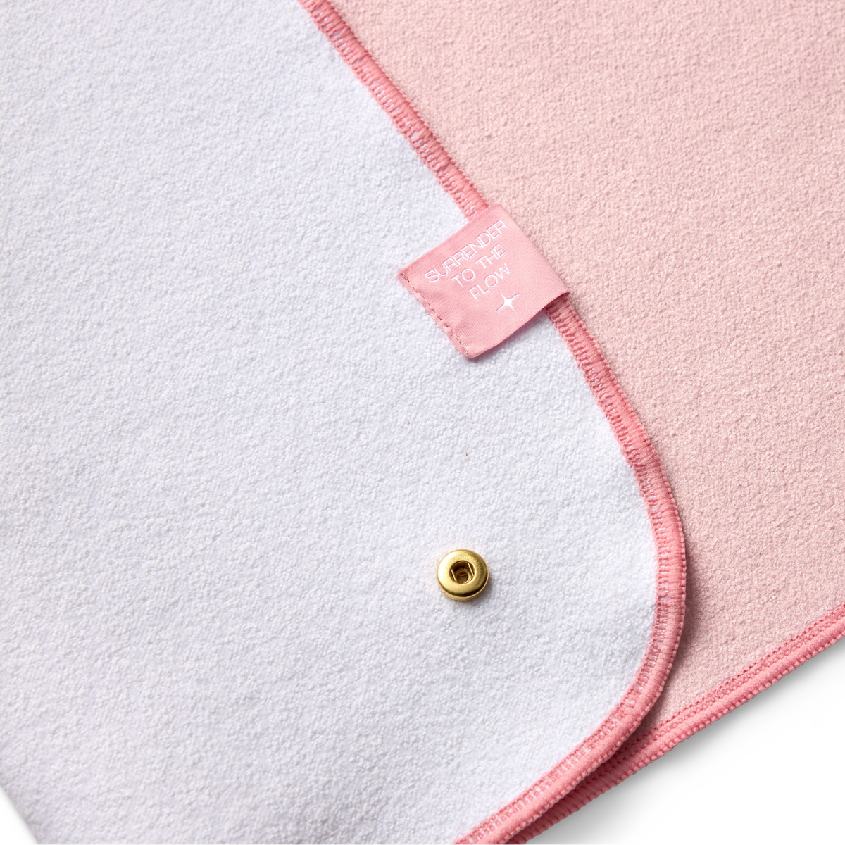 Pink yoga mat towel folded over showing with a gold button and label on a white background