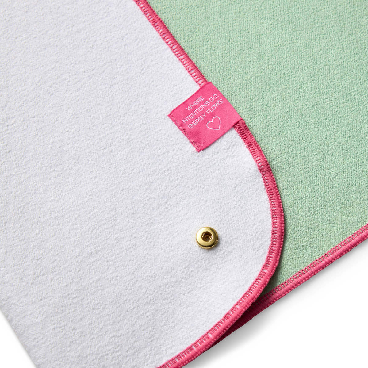 Close-up of a folded green towel folded over to show backside with a pink label and gold button