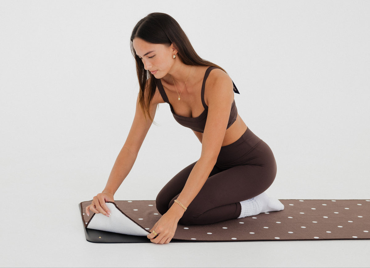 woman in brown athletic gear snapping brown/polka dot yoga mat towel to yoga mat
