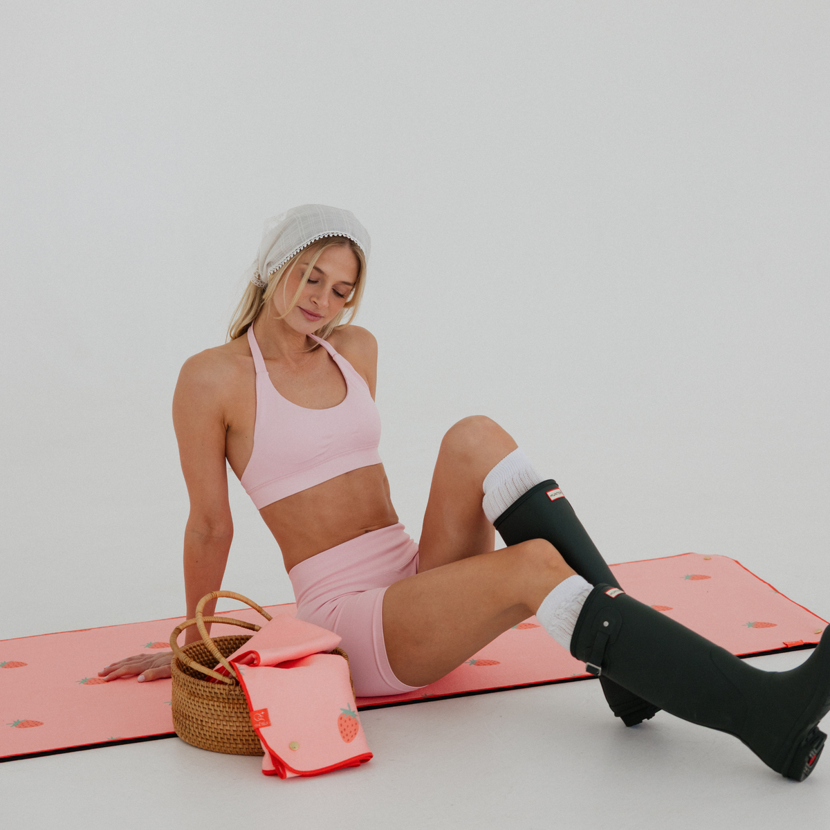 model sitting on pink yoga mat towel with strawberry print and green rainboots with basket