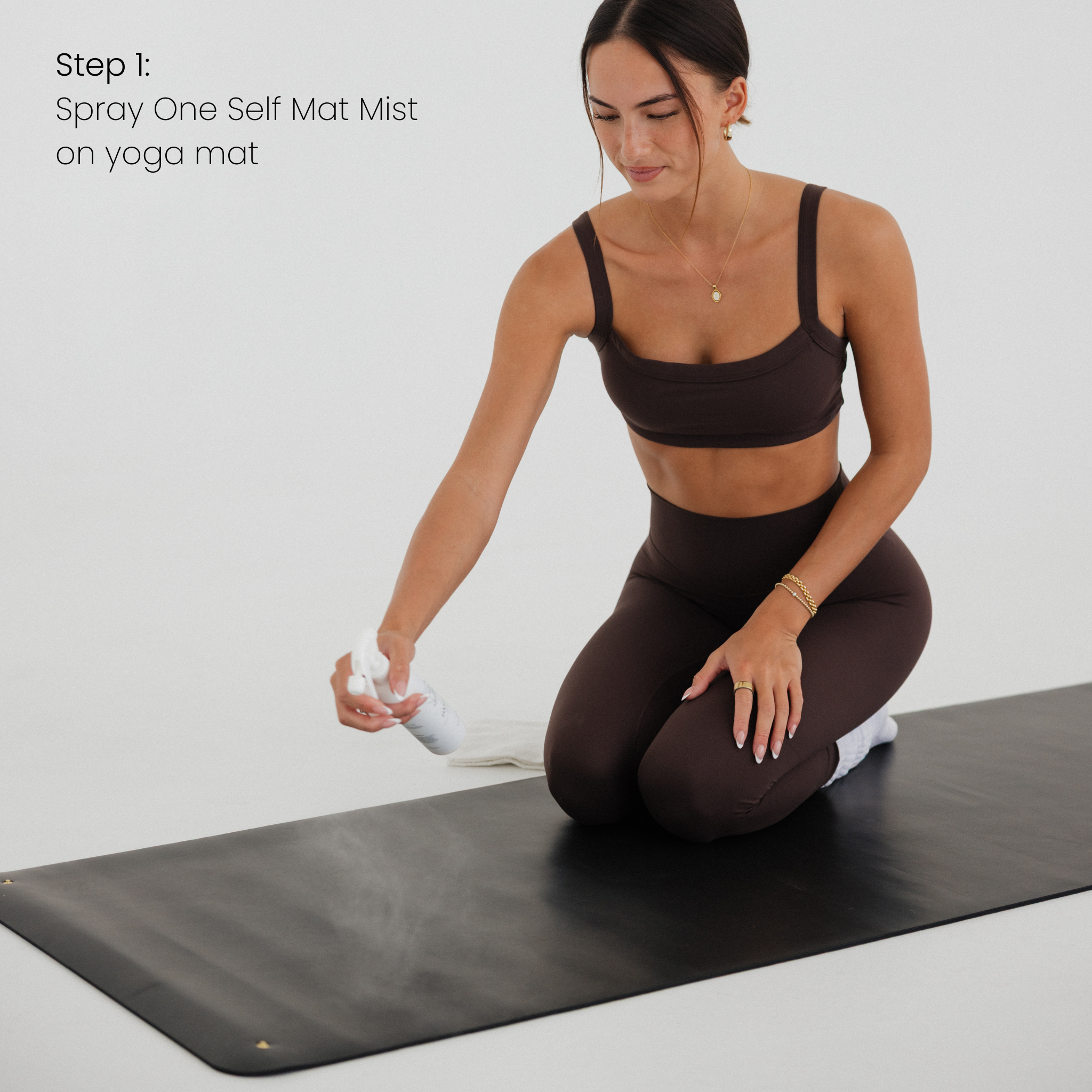 Woman misting a yoga mat with a spray bottle on a plain background
