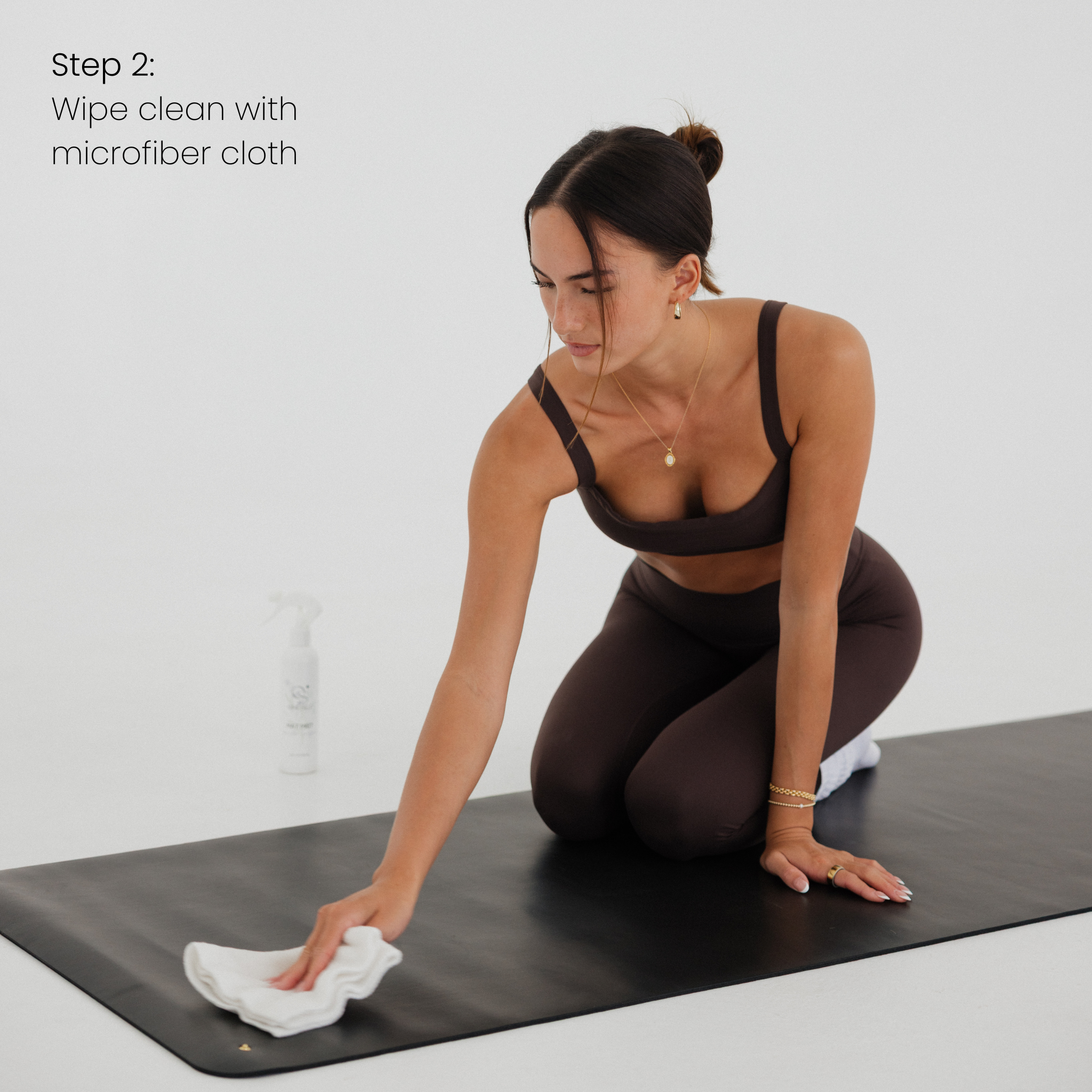 Woman cleaning a yoga mat with a microfiber cloth on a white background