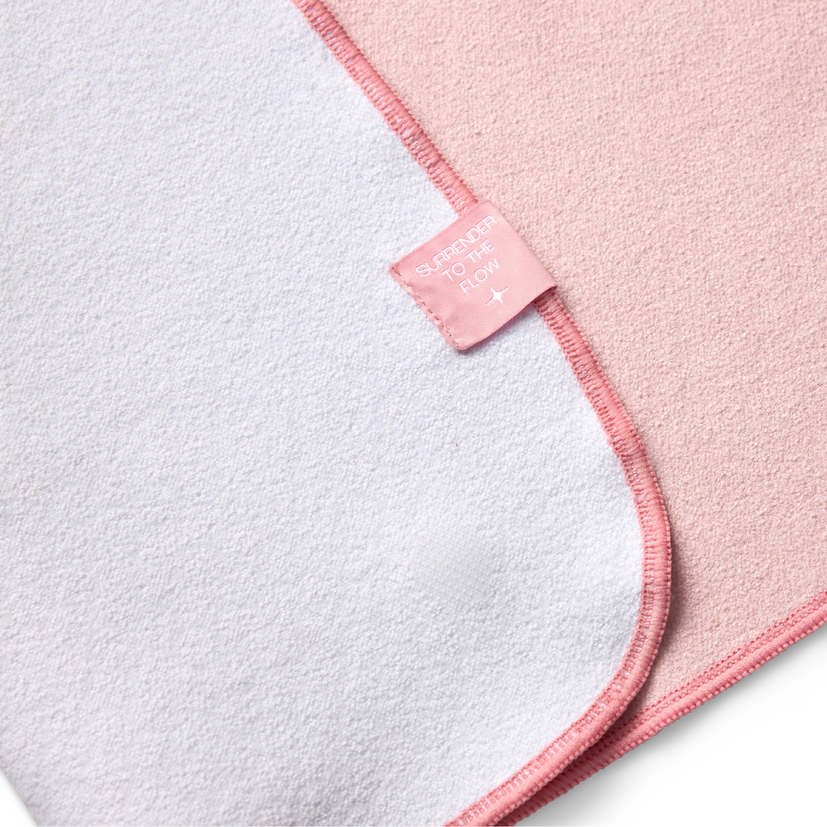 pink yoga mat towel folded to show white back with tag that says "surrender to the flow"