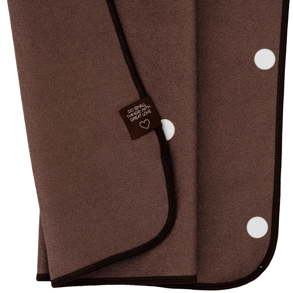 Dark brown hand towel with white polka dots. Towel folded to show tag that states "do small things with great love"