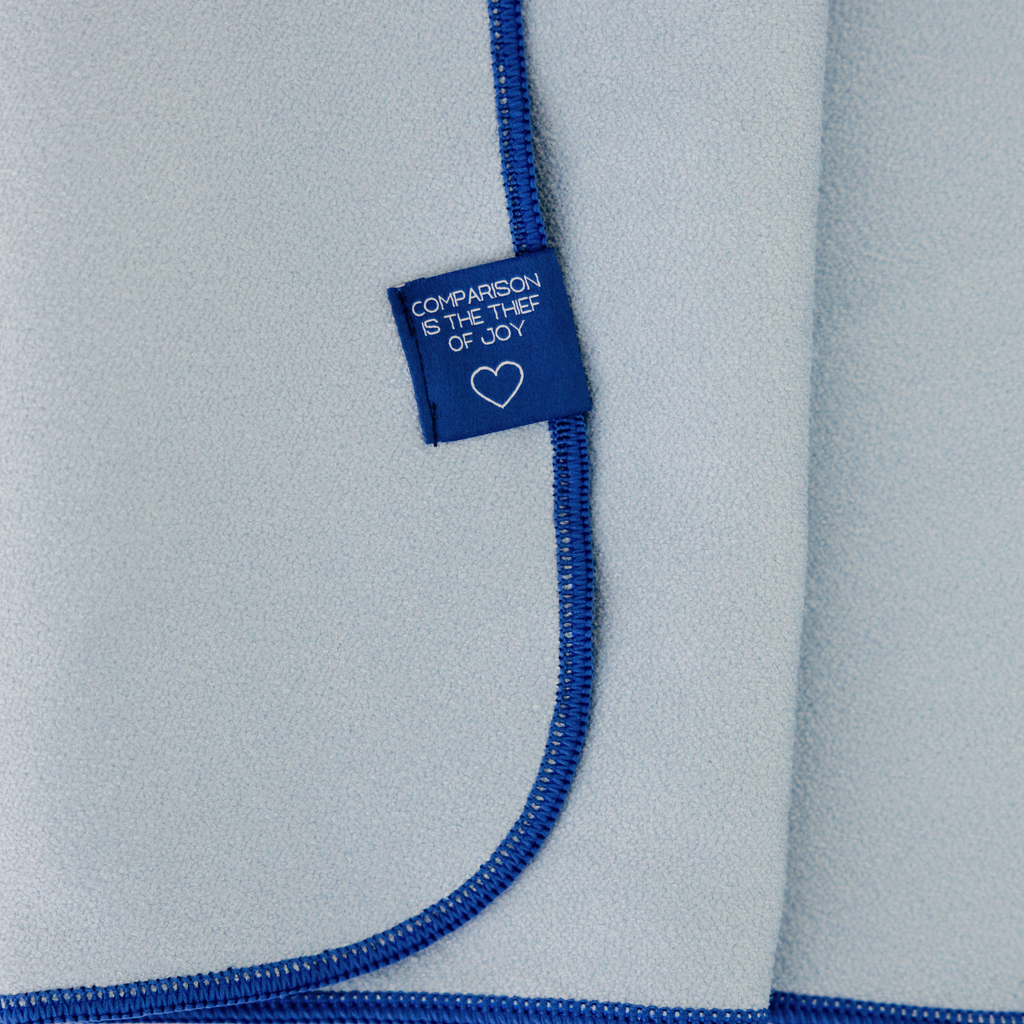 blue hand towel with fold tag that says "comparison is the thief of joy"