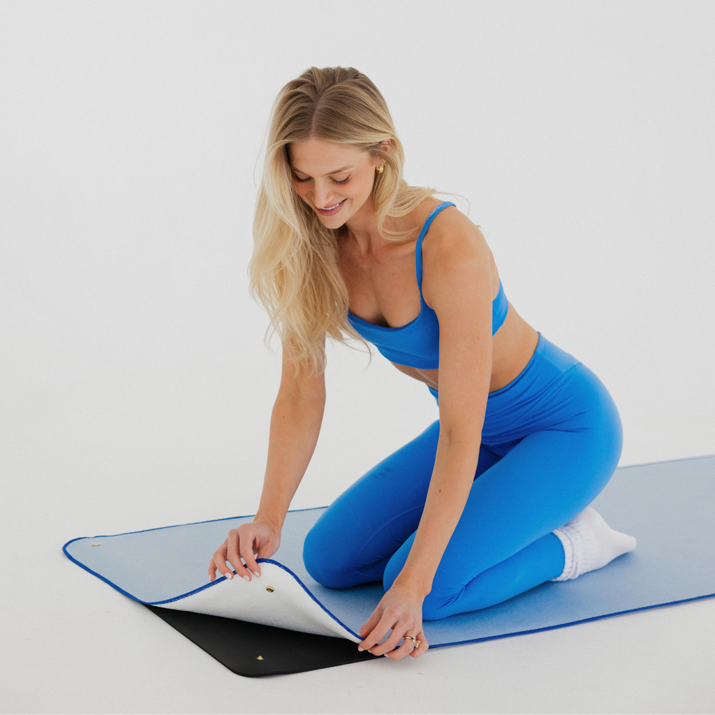 model kneeling on yoga mat towel snapping blue towel onto black mat