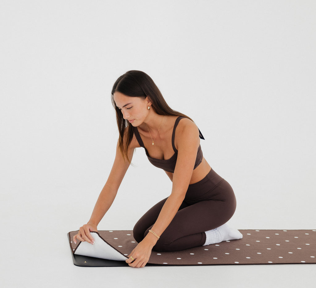 woman in brown athletic gear snapping brown/polka dot yoga mat towel to yoga mat