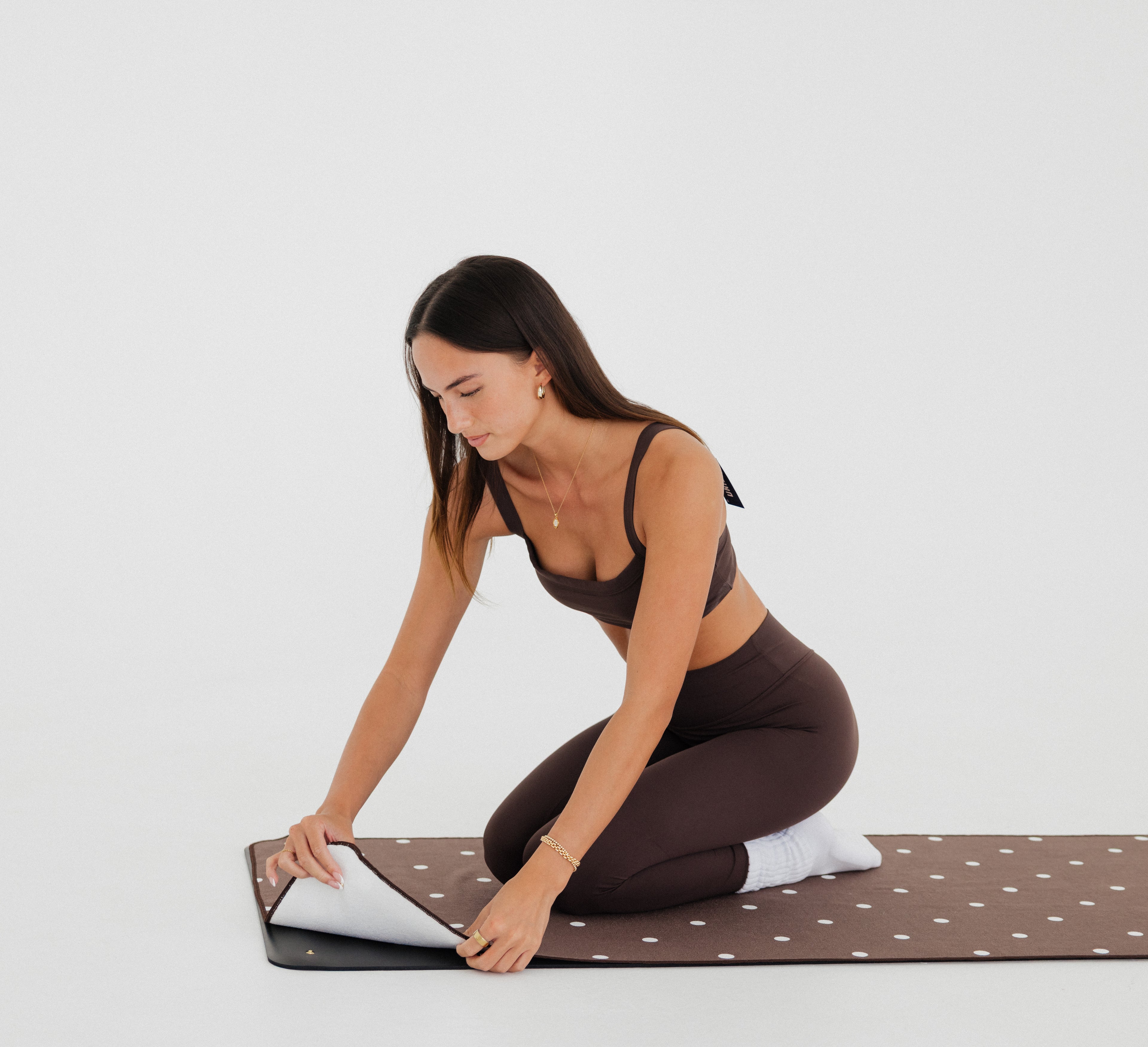 woman in brown athletic gear snapping brown/polka dot yoga mat towel to yoga mat