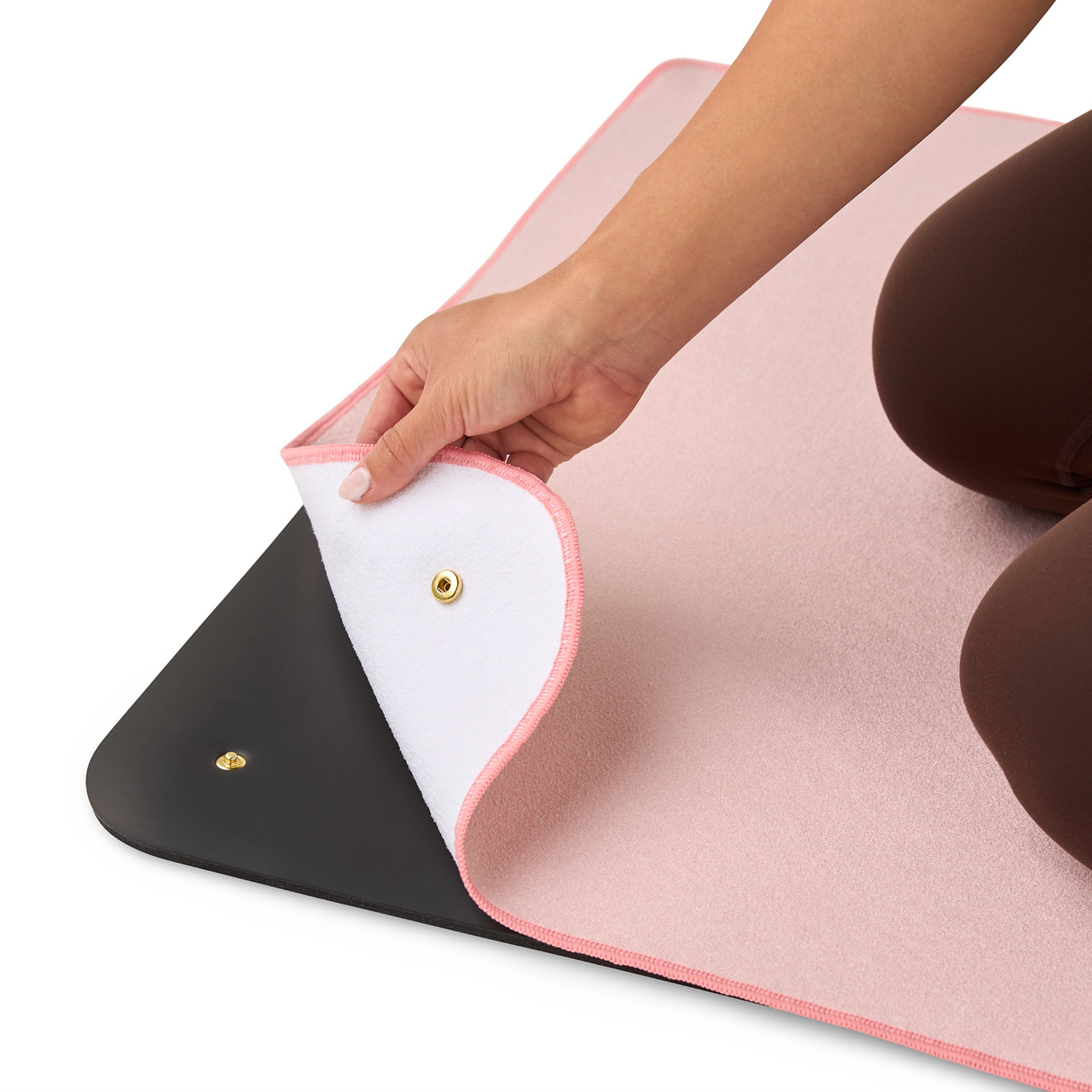 Person holding a pink yoga mat towel kneeling on black yoga mat showing snap mechanism